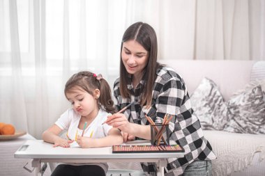 Çocuklu bir anne masada oturur ve ödev yapar. Çocuk evde öğreniyor. Evde eğitim. Metin için boşluk.