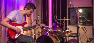 Kayıt stüdyosunda elektro gitar çalan bir adam. Arka planda davul seti olan müzisyenler için bir prova odası. Müzikal yaratıcılık kavramı.