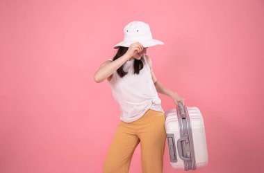 Şık yaz kıyafetleri içinde şık bir kadının portresi pembe arka planda beyaz bir şapka ve seyahat için bavul. Yaz turizmi kavramı.