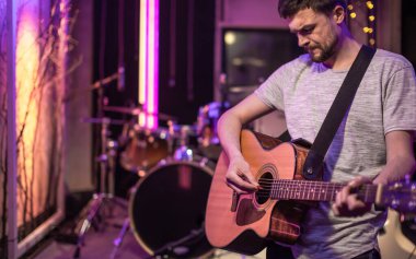 Kayıt stüdyosunda akustik gitar çalan bir adam. Müzisyenlerin provaları için arka planda davul seti olan bir oda. Müzikal yaratıcılık ve gösteri dünyası kavramı..