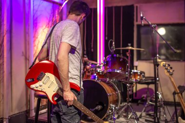 Kayıt stüdyosunda elektro gitar çalan bir adam. Arka planda davul seti olan müzisyenler için bir prova odası. Müzikal yaratıcılık kavramı.