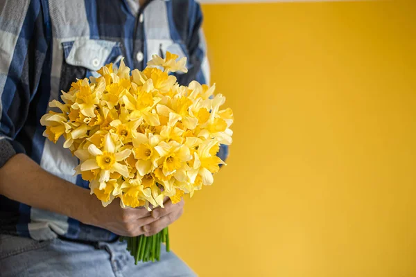 Hipster-a man on a yellow background in a shirt and a large bouquet of daffodils. The concept of greetings and women\'s day.