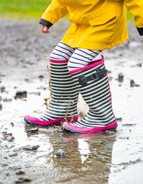 Lastik çizmeli bir çocuk su birikintisine atlıyor. Kapatın. Sonbahar-yaz konsepti