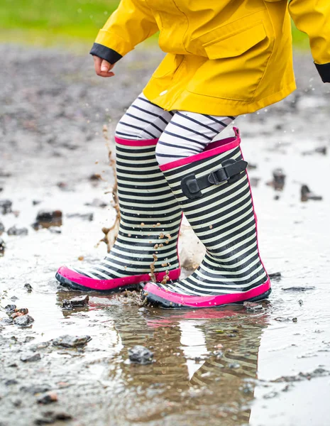 Lastik çizmeli bir çocuk su birikintisine atlıyor. Kapatın. Sonbahar-yaz konsepti
