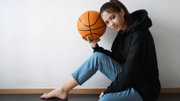 Genç güzel kız basketbol oyuncusu katta oturan ve topu tutan poz