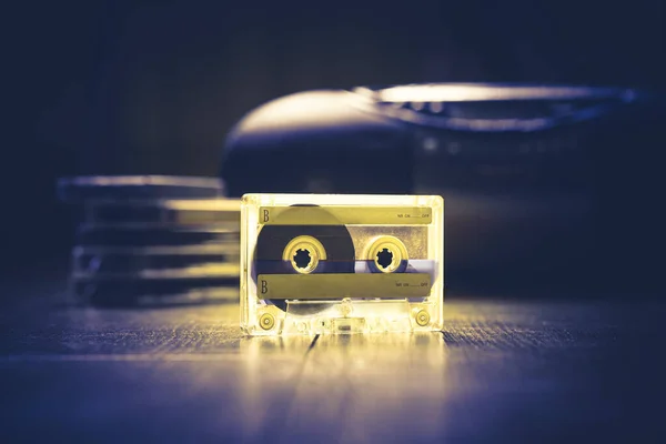 Transparent audio cassette tape lit by yellow and blue lamps. Retro tape recorder on the background. Retro audio. Hipster fashion concept. Lockdownart
