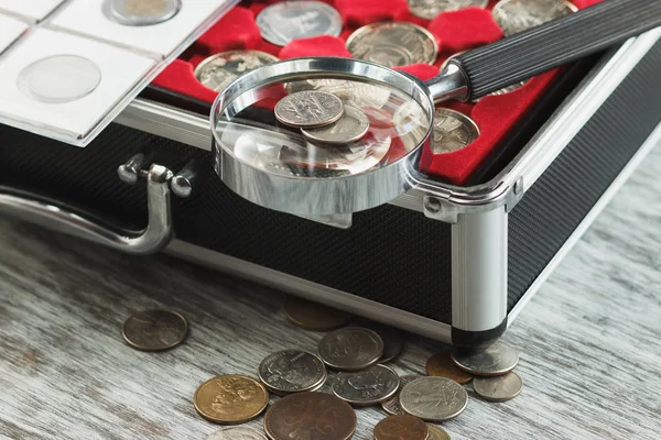 Different collector's coins in the box with a magnifying glass — Stock Photo, Image