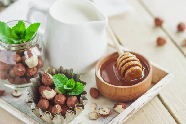 Honung i trä bowl, mynta blad, hasselnötter och burk med mjölk — Stockfoto