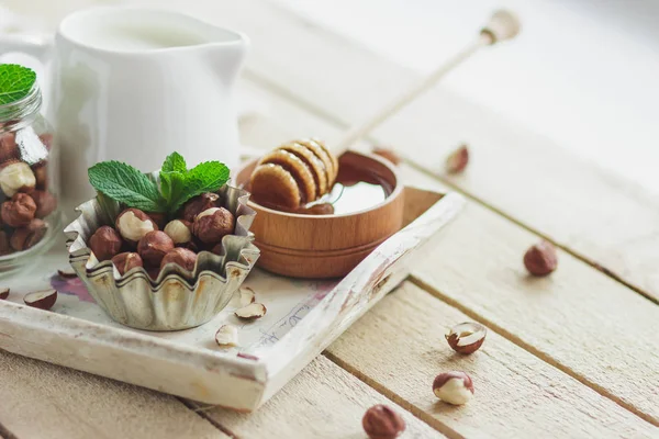 Honung i trä bowl, mynta blad, hasselnötter och burk med mjölk — Stockfoto