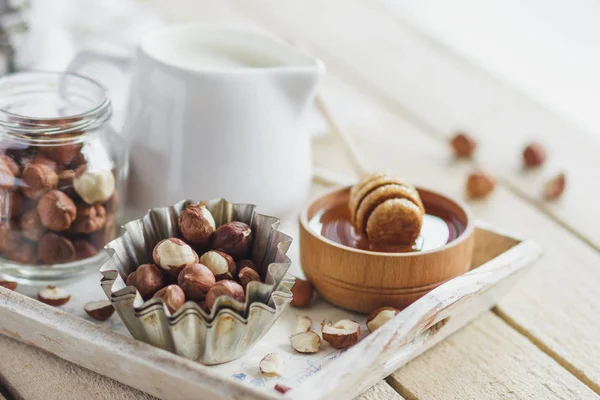 Honung i trä skålen, hasselnötter och burk med mjölk i trä facket — Stockfoto