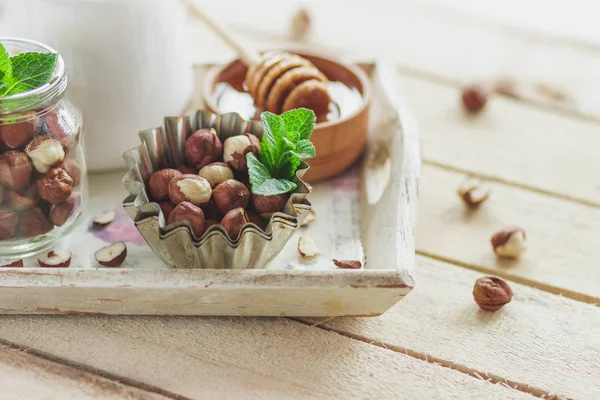 Honung i trä bowl, mynta blad, hasselnötter och burk med mjölk i trä facket — Stockfoto