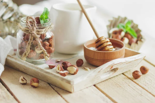 Honung i trä bowl, mynta blad, hasselnötter och burk med mjölk i trä facket — Stockfoto