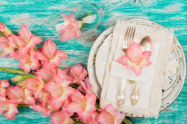 Tableware and silverware with light pink gladiolus on the azure background — Stock Photo, Image