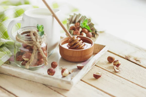 Honung i trä bowl, mynta blad, hasselnötter och burk med mjölk i trä facket — Stockfoto