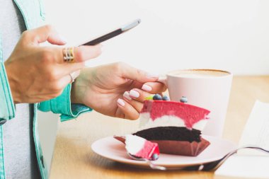 Kadın bir resim Kupası cappuccino ve tatlı bir parça ile plaka üzerine alır.