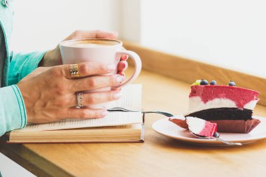 Bir fincan kapuçino ve tatlı plaka üzerinde bir parçası olan kadın