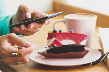 Kadın bir resim Kupası cappuccino ve tatlı bir parça ile plaka üzerine alır.