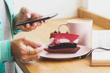 Kadın bir resim Kupası cappuccino ve tatlı bir parça ile plaka üzerine alır.