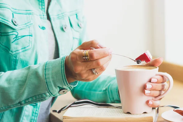 Bir fincan kapuçino ve tatlı plaka üzerinde bir parçası olan kadın