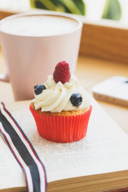 Ahududu ve kitap, sıcak cappuccino bardak yaban mersini ile küçük cupcake