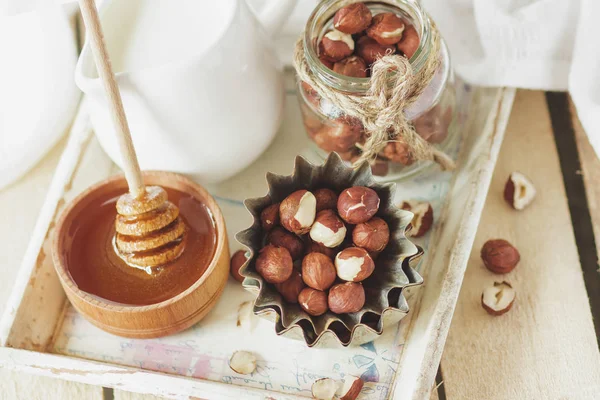 Honung i trä skålen, hasselnötter och burk med mjölk i trä facket — Stockfoto