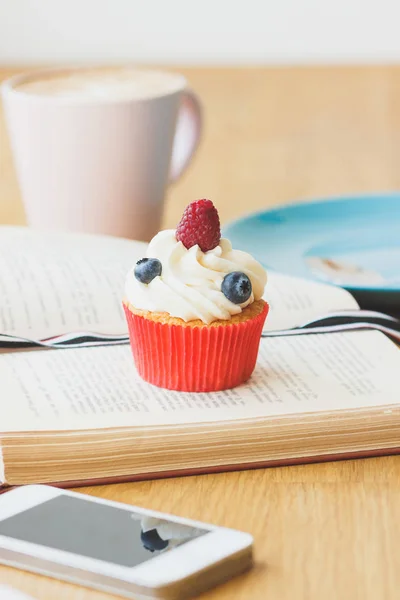 Petit cupcake aux framboises et bleuets sur le livre, tasse de h — Photo