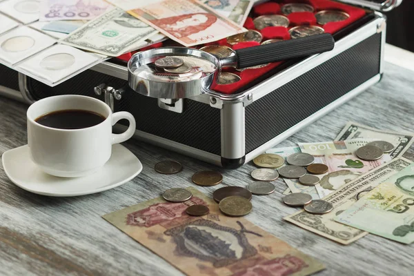 Різні колекційні монети та банкноти, чашка кави та збільшувальний келих — стокове фото
