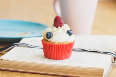 Ahududu ve kitap, sıcak cappuccino bardak yaban mersini ile küçük cupcake