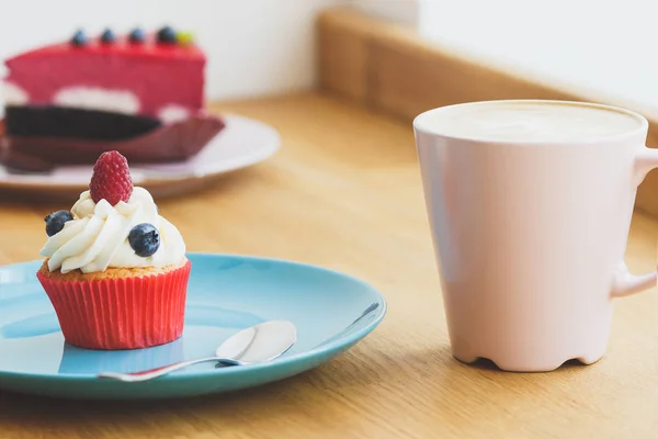 Petit cupcake aux framboises et bleuets dans l'assiette, tasse de cappuccino chaud — Photo