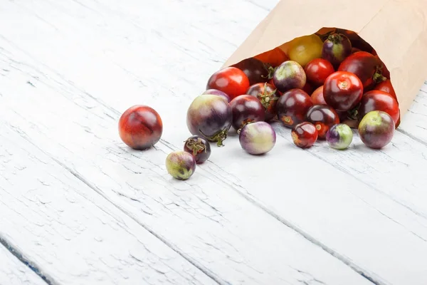Different tomatoes in the paper bag on the white wooden background