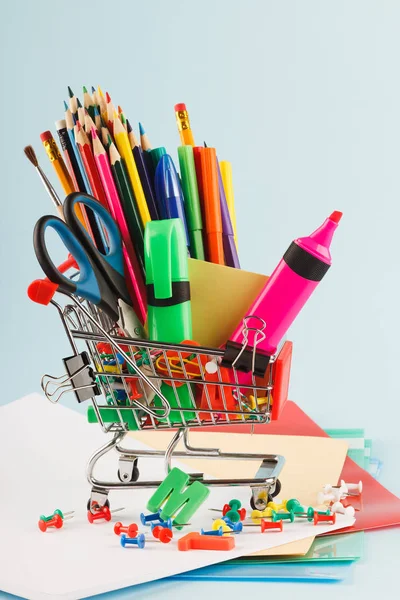 Carrinho de compras com diferentes artigos de papelaria, fundo azul claro — Fotografia de Stock