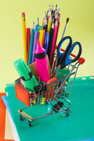 Carro de compras con diferentes artículos de papelería, fondo amarillo claro — Foto de Stock