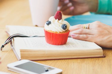 Ahududu ve yaban mersini, kitap ve fincan sıcak cappuccino küçük cupcake