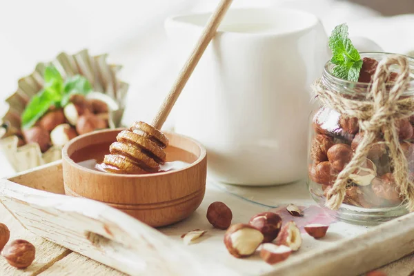 Honung i trä bowl, mynta blad, hasselnötter och burk med mjölk i trä facket — Stockfoto