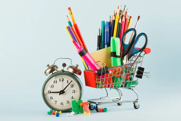 Carro de compras con diferentes artículos de papelería, fondo azul claro — Foto de Stock