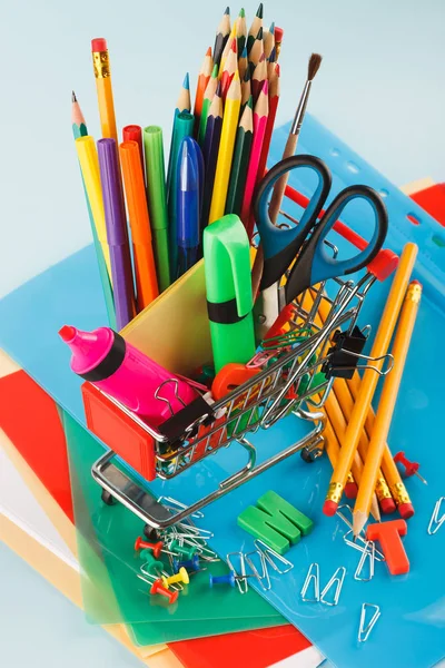 Carro de compras con diferentes artículos de papelería, fondo azul claro — Foto de Stock