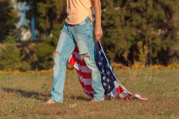 Woman with a flag of United States of America in the hand, outdoors, soft focus background