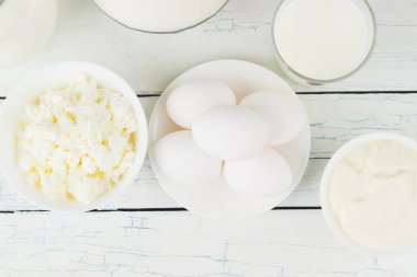 Beyaz ahşap tahtalarda farklı süt ürünleri, üst manzara.