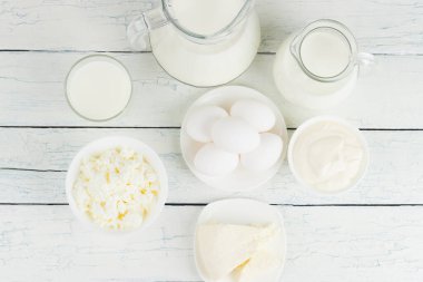 Beyaz ahşap tahtalarda farklı süt ürünleri, üst manzara.