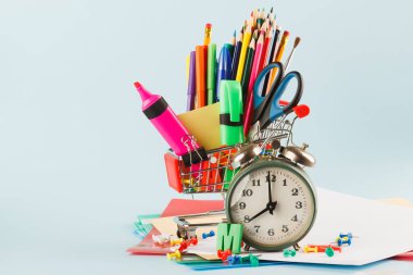 Açık mavi arka planda farklı kırtasiye malzemesi olan alışveriş arabası.