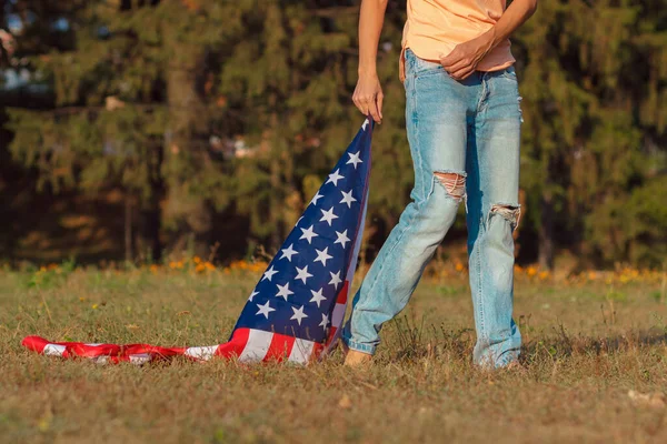 Woman with a flag of United States of America in the hand, outdoors, soft focus background