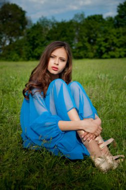 çimenlerin üzerinde elleriyle cross-legged oturan üzgün kız. Elbise