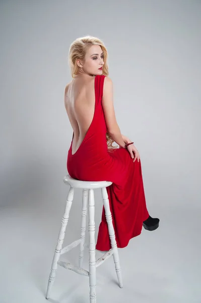Modell i lång röd frack sitter med vikta ben korsade — Stockfoto