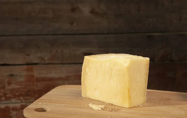 一块硬的Parmesan奶酪躺在一块木板上 棕色的背景 在一个水平的框架上有一个文字的地方 — 图库照片
