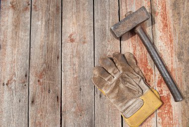 Paslı metal çekiç ve kirli iş eldivenleri ahşap bir sırt deliğinde yatıyor.