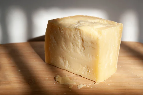一块巨大的带有锯齿状边缘的硬Parmesan奶酪躺在木板上 碎屑散落在附近 阳光下形成的阴影 — 图库照片