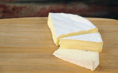 Tahta bir tahtanın üzerinde üç dilime ayrılmış yumuşak brie peyniri var. Krema renginde narin bir krem peyniri.