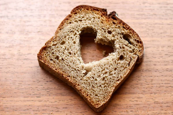 Pezzo di pane integrale scuro con cuore su sfondo di legno — Foto Stock