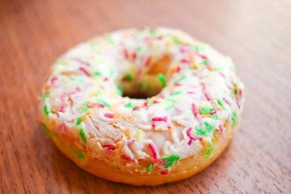 Donut with white icing and sprinkles on wooden background table — Stock Photo, Image