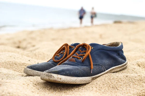 Simple blue men shoes with brown laces on sand on beach. Two peo Royalty Free Stock Photos